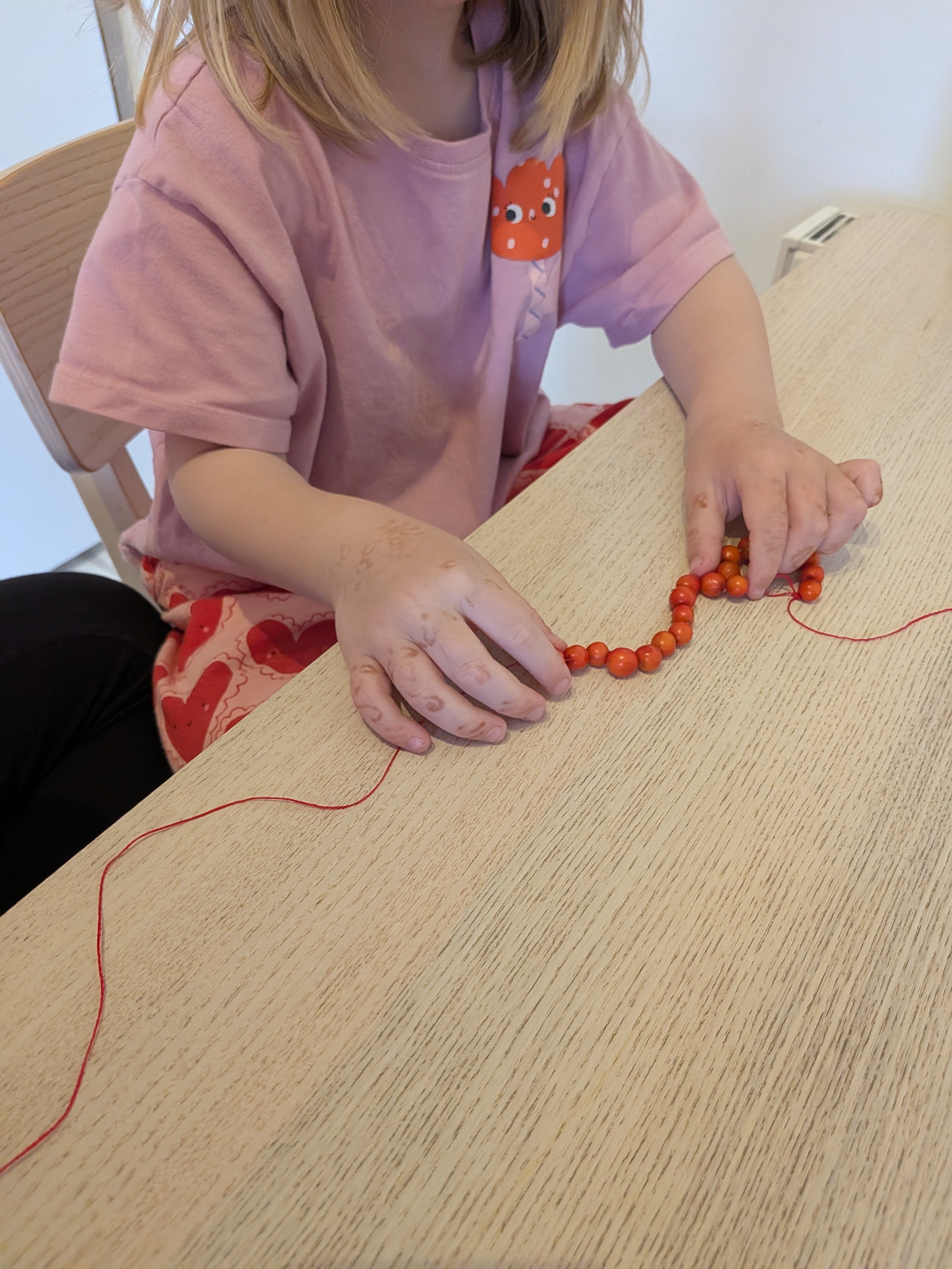 A child threading rowan berries onto red thread