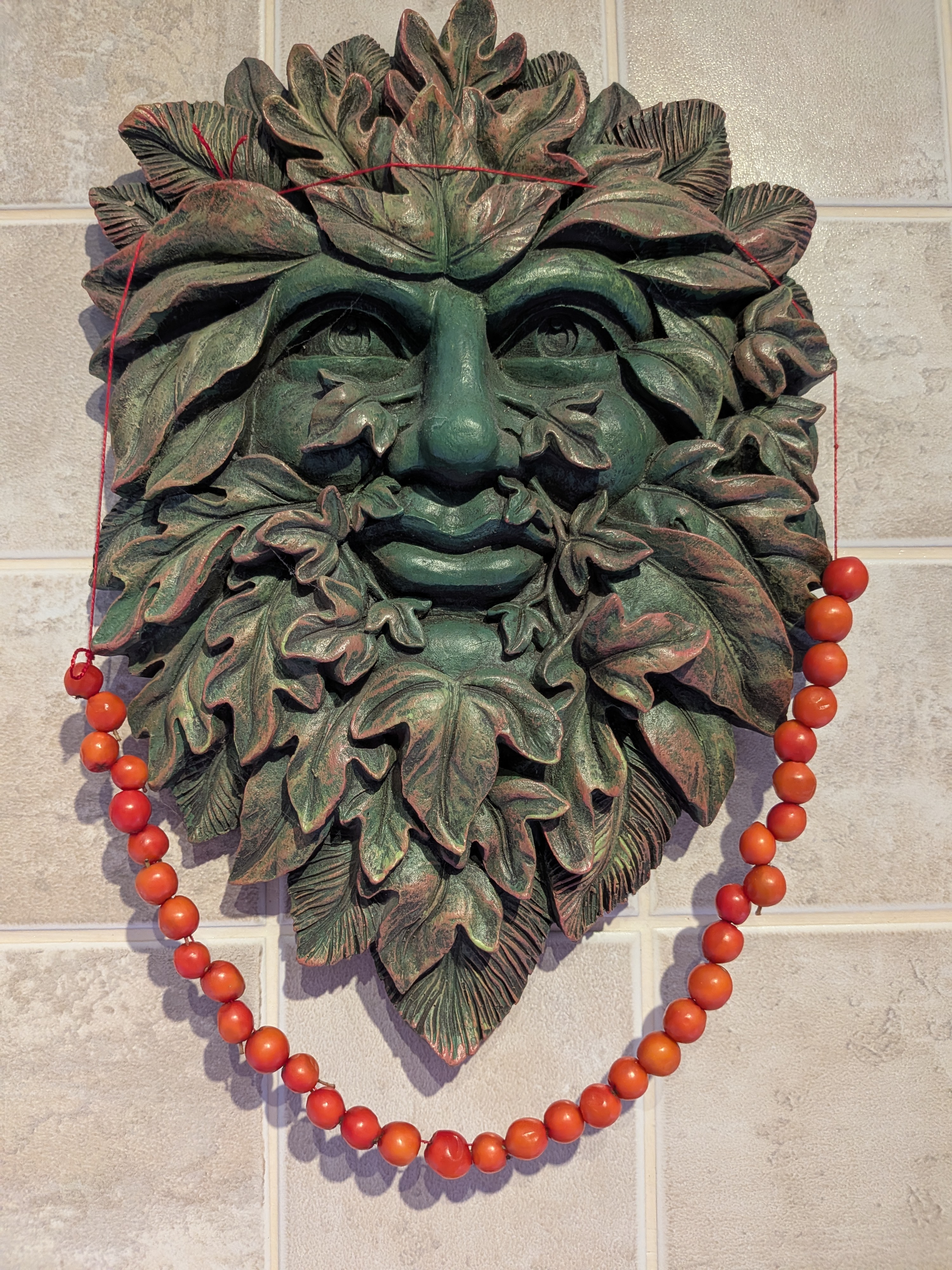 A finished string of rowan berries draped around a Green Man wall plaque