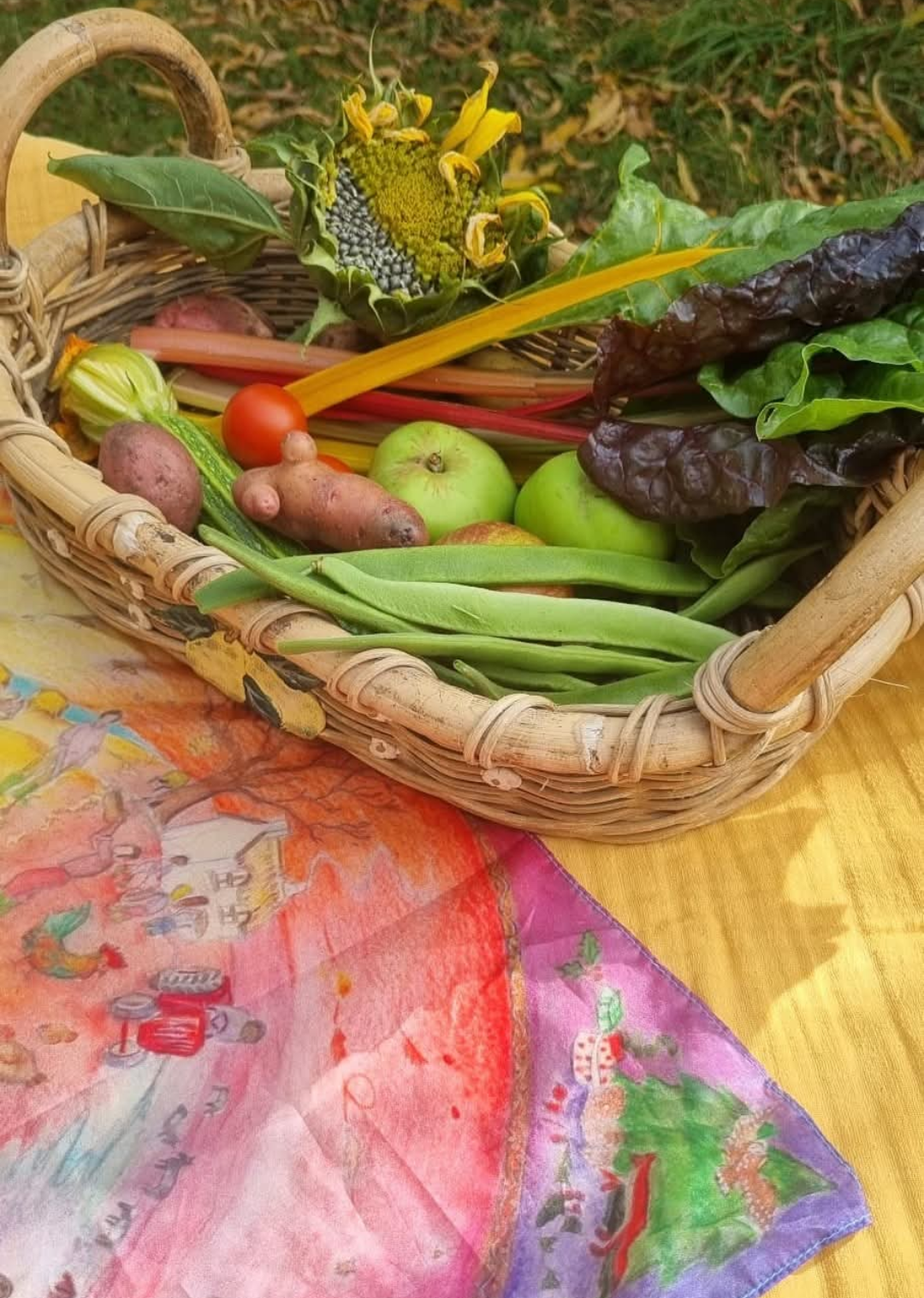 A woven basket of seasonal harvest (vegetables, fruit and a sunflower head) on a hand-painted cloth